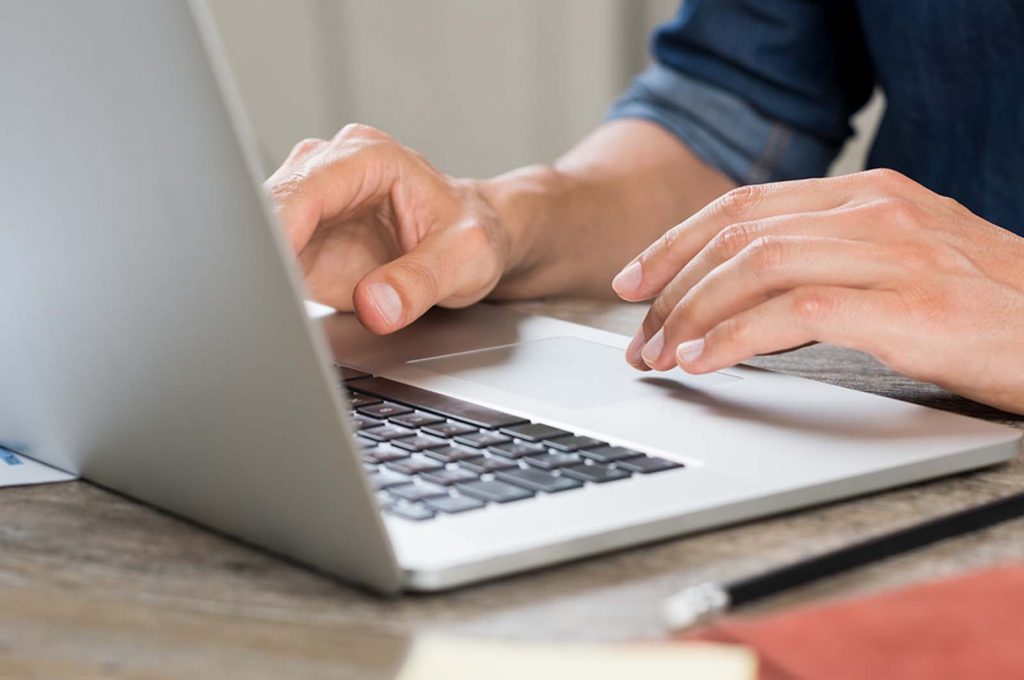 Closeup hand of businessman using laptop at office. Close up view of man hands working on laptop while sitting at wooden desk. Closeup of casaul worker typing on laptop computer and surfing internet.