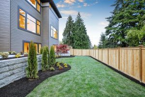 Luxurious contemporary three-story wood siding home exterior in Bellevue. Nice backyard landscape with well-kept lawn flower beds and wooden fence. Northwest USA