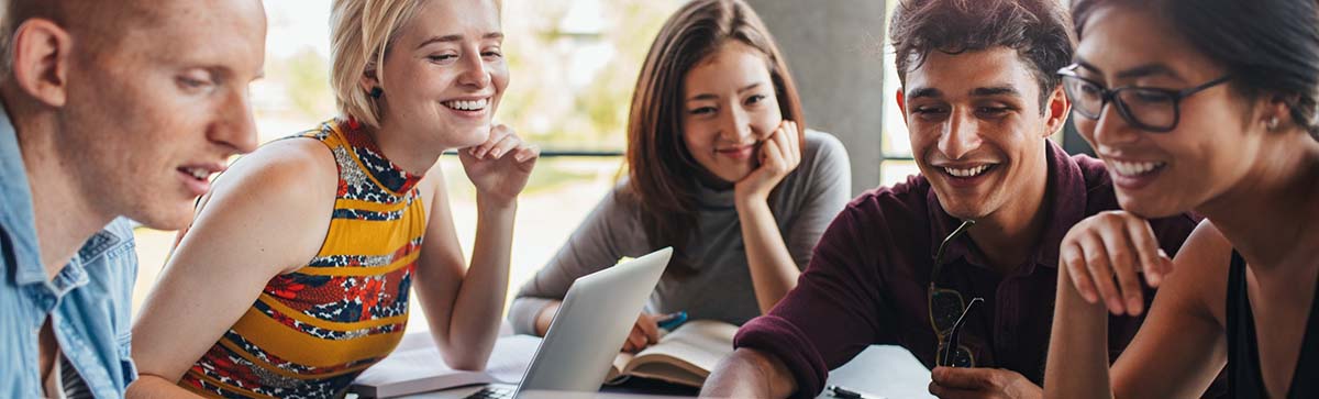 Multiracial group of young students studying in the library. Young people sitting together at table with books and laptop for researching information for their project.